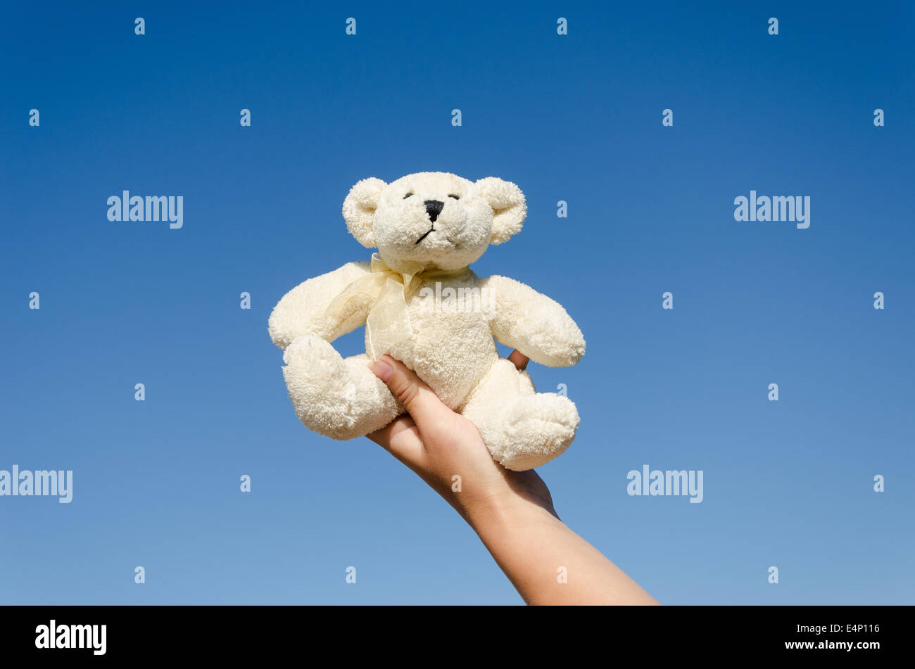 Piccolo, grazioso fluffy orsacchiotto giocattolo in mano sul cielo blu sullo sfondo Foto Stock