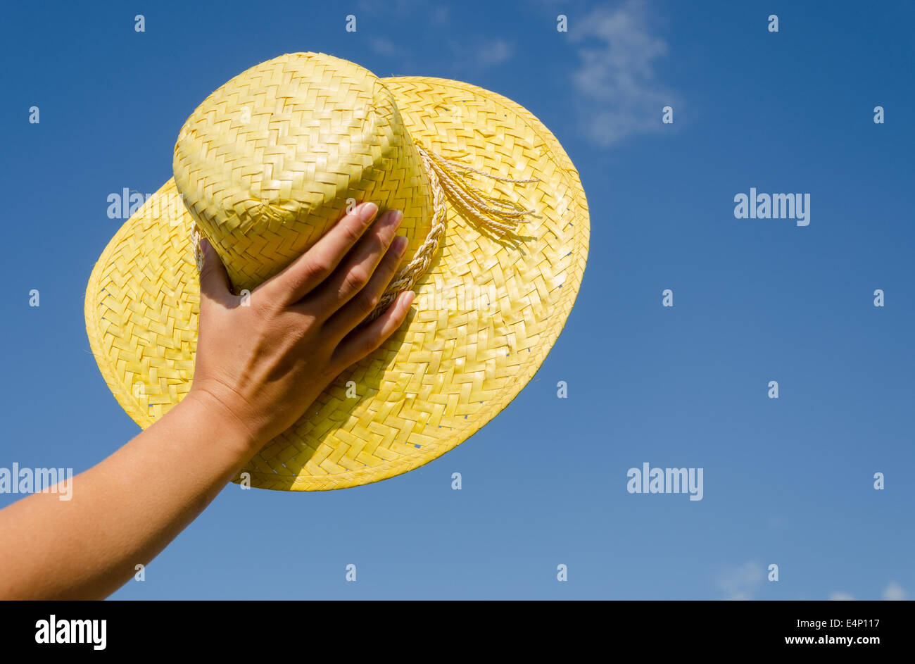 Tenere in mano femminile giallo paglia rifugio estivo sul cielo blu sullo sfondo Foto Stock