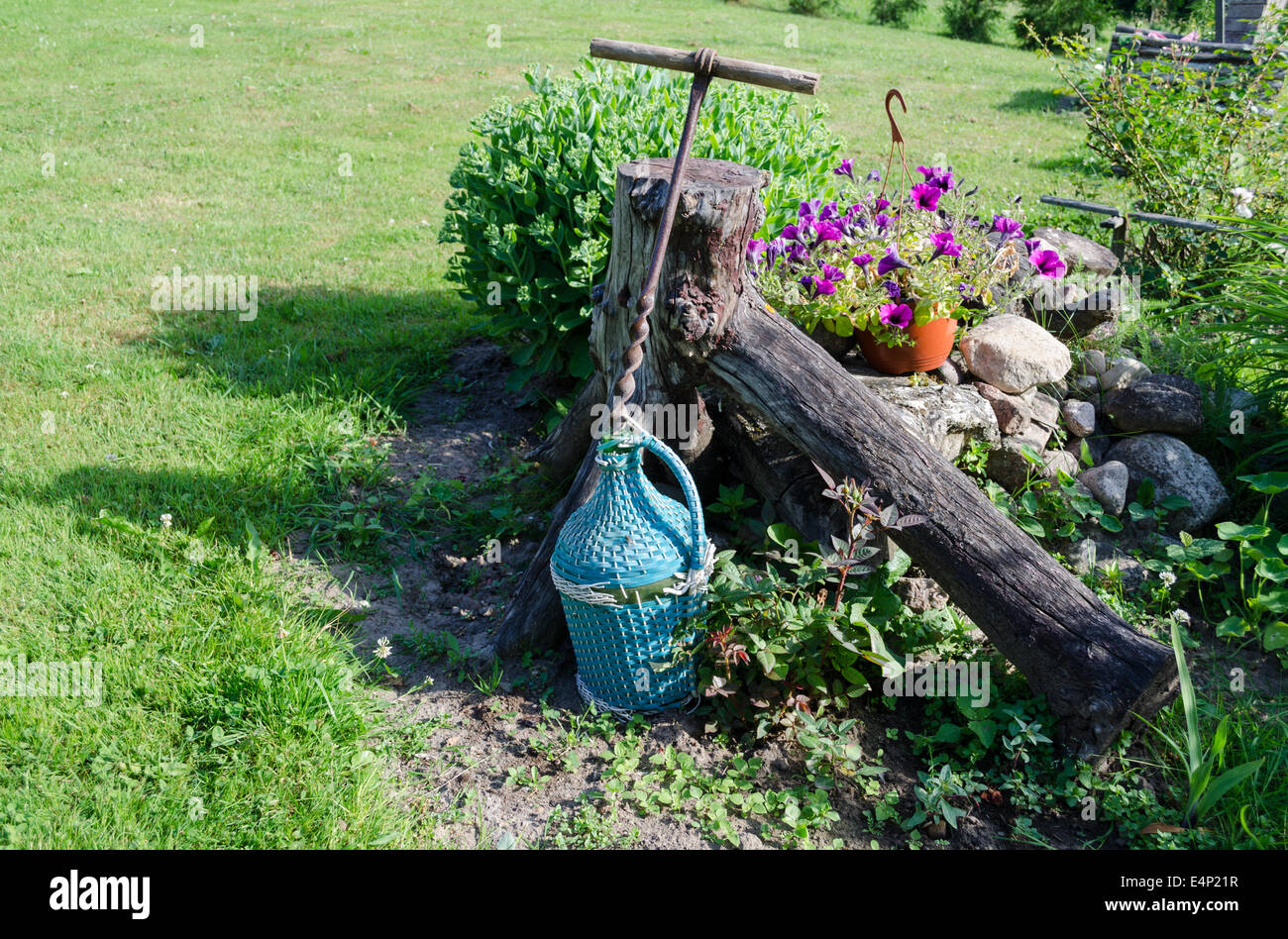 Grande bottiglia di vino avvolto in plastica blu ramoscelli e grande stilizzata assolcatore di ferro nei pressi di erba di fiori Foto Stock