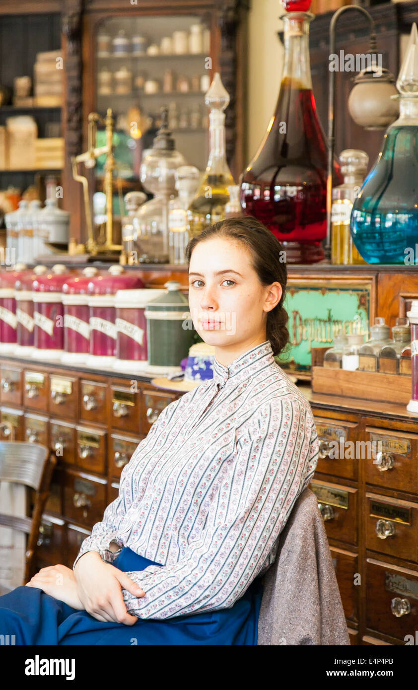 Giovane donna assistente vendite seduto in farmacia vittoriano/ farmacia, a Blists Hill Città Vittoriano museum, England Regno Unito Foto Stock