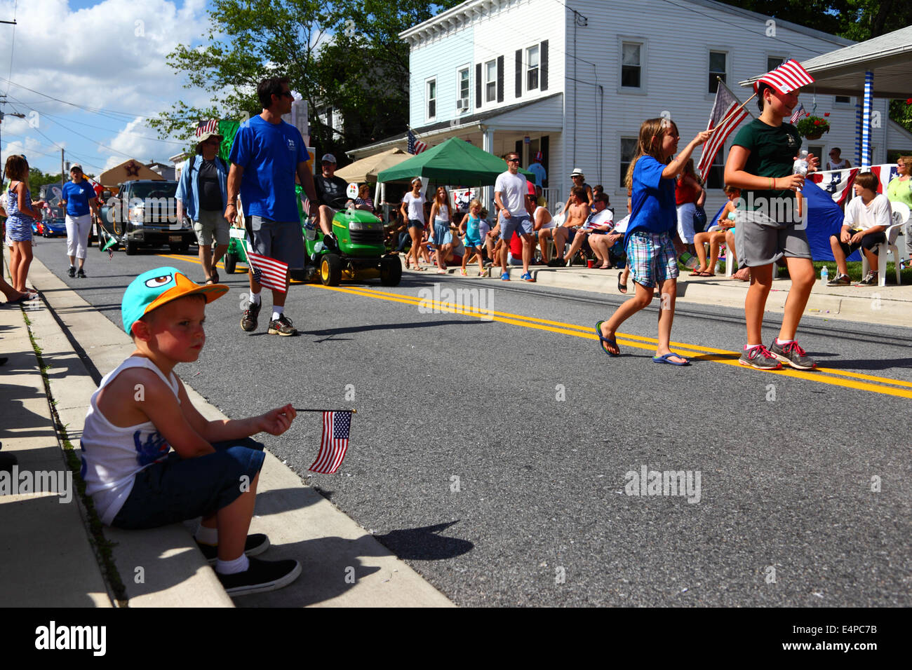 Annoiato ragazzo seduto su un marciapiede azienda America bandiera durante il 4 di luglio il Giorno di Indipendenza parate, Catonsville, Maryland, Stati Uniti d'America Foto Stock