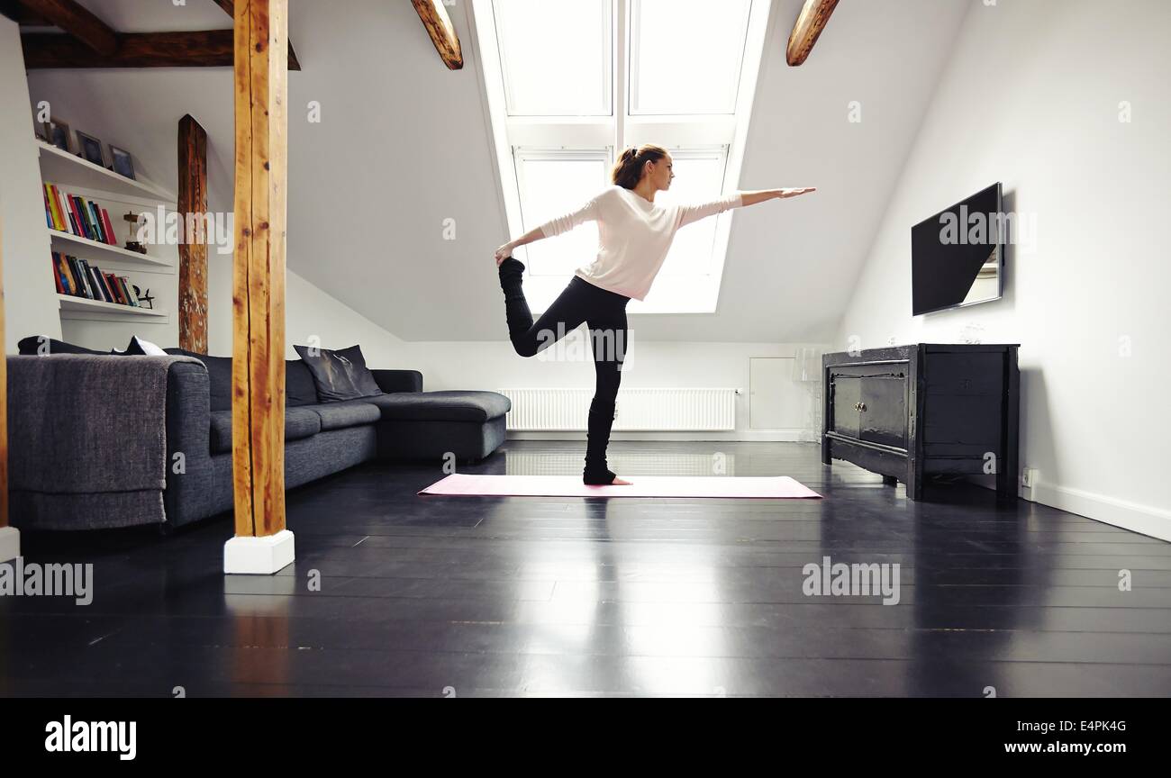 Lunghezza completa immagine di montare la giovane donna a praticare yoga a casa. Sano giovane donna che esercitano nel soggiorno. Modello caucasico. Foto Stock