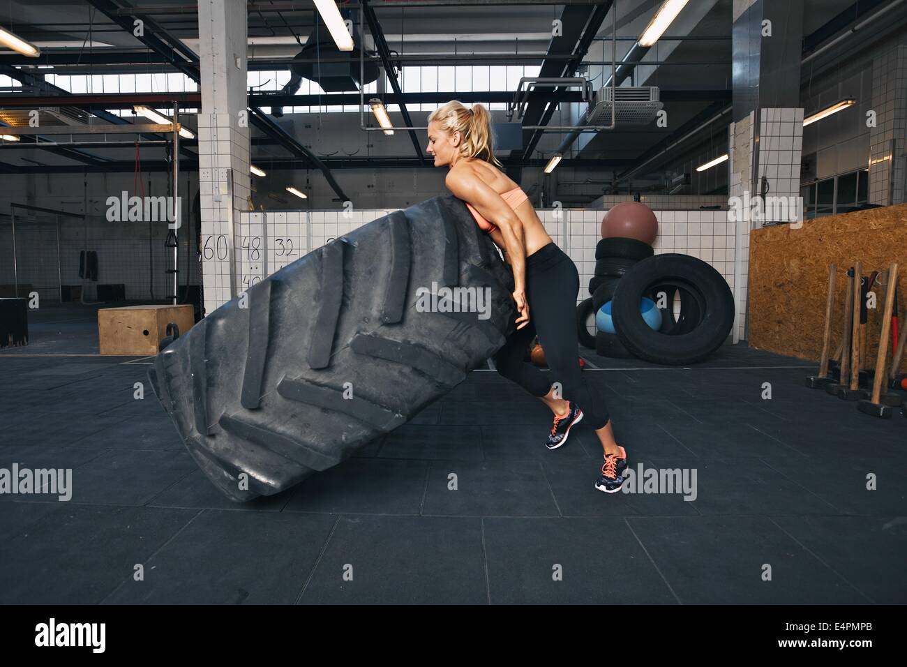 Montare atleta femminile capovolgimento di un enorme pneumatico. Muscolare di giovane donna crossfit facendo esercizio in palestra. Foto Stock