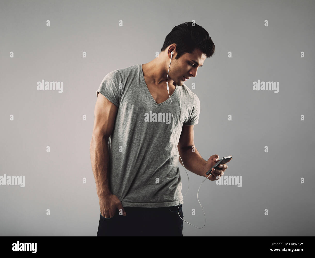 Bel giovane in t-shirt casual ascoltando la musica sul telefono cellulare. Ispanico modello maschile che indossa gli auricolari e ascolto di musica Foto Stock