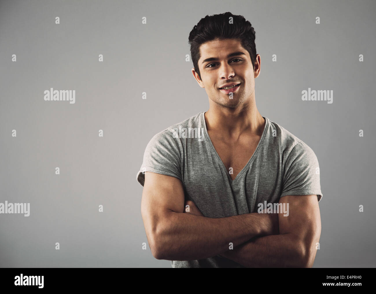 Ritratto di bel giovane uomo in piedi con le braccia incrociate contro uno sfondo grigio con copia spazio. Ispanico moda maschile mod Foto Stock