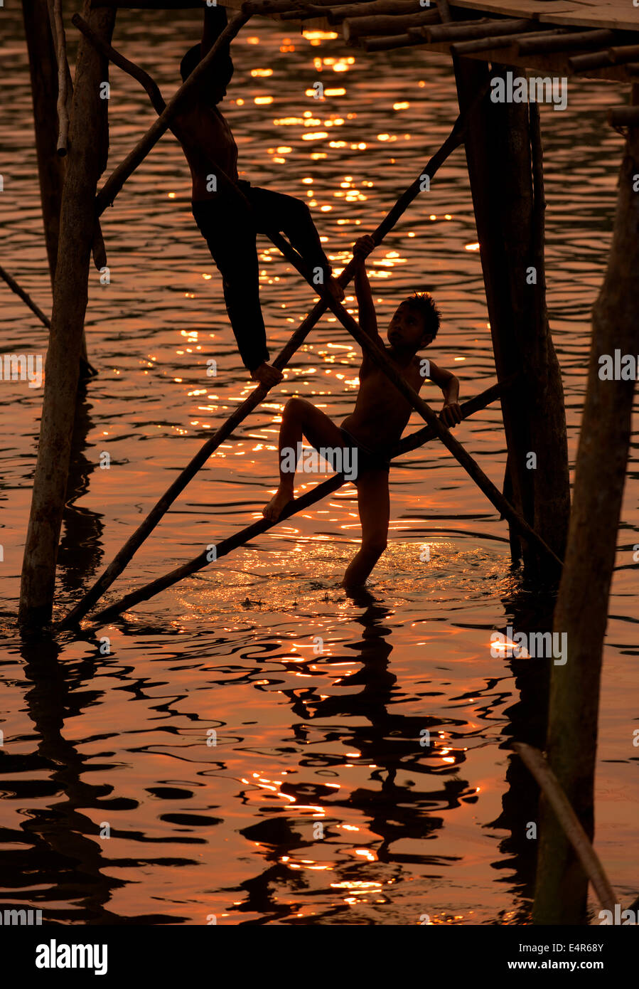 Ragazzi arrampicata sulla struttura di un ponte di bambù durante il tramonto in Vang Vieng. Foto Stock