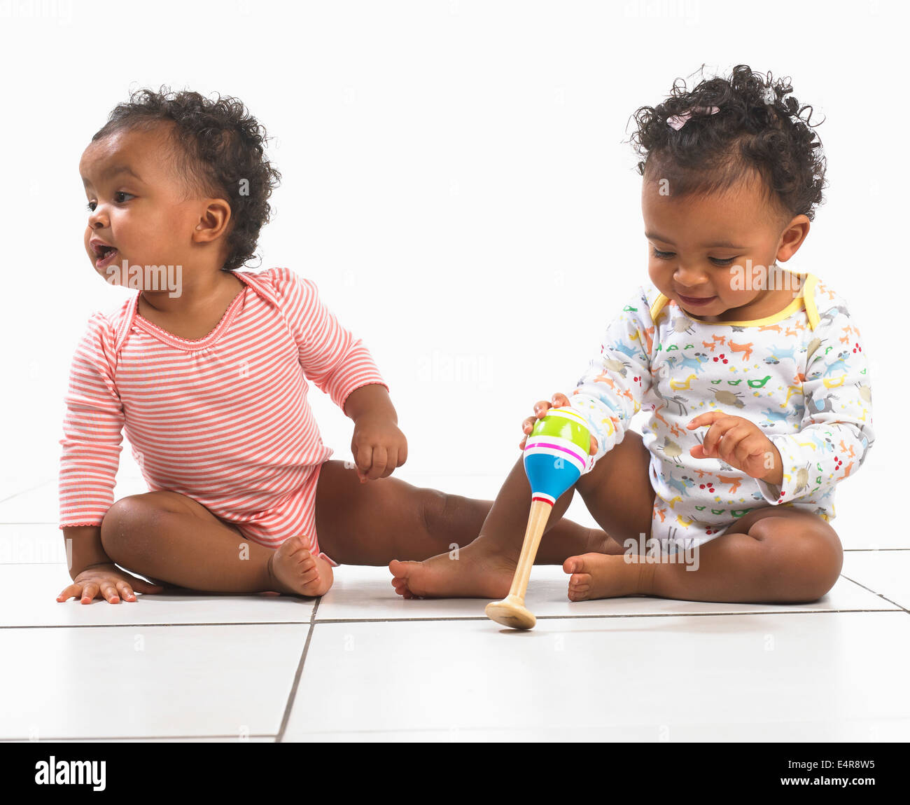 Twin un ragazzo e una ragazza (18 mesi) seduto sul pavimento, uno tenendo un maraca Foto Stock