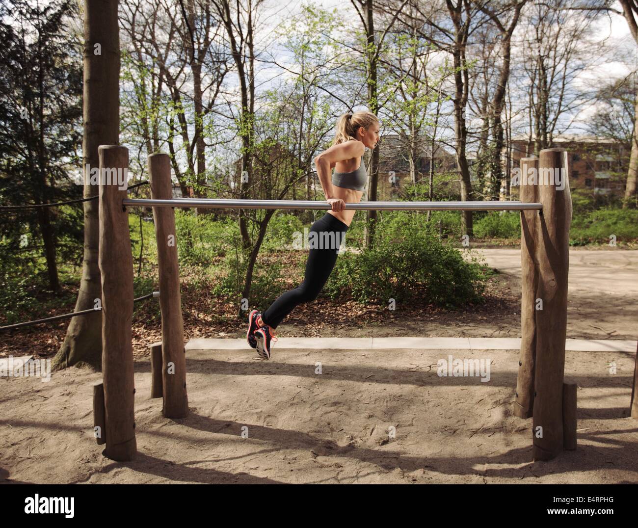 Vista laterale della muscolatura giovane donna facendo tricipiti dips su barre parallele al parco. Femmina caucasica modello fitness esercizio outdoor Foto Stock