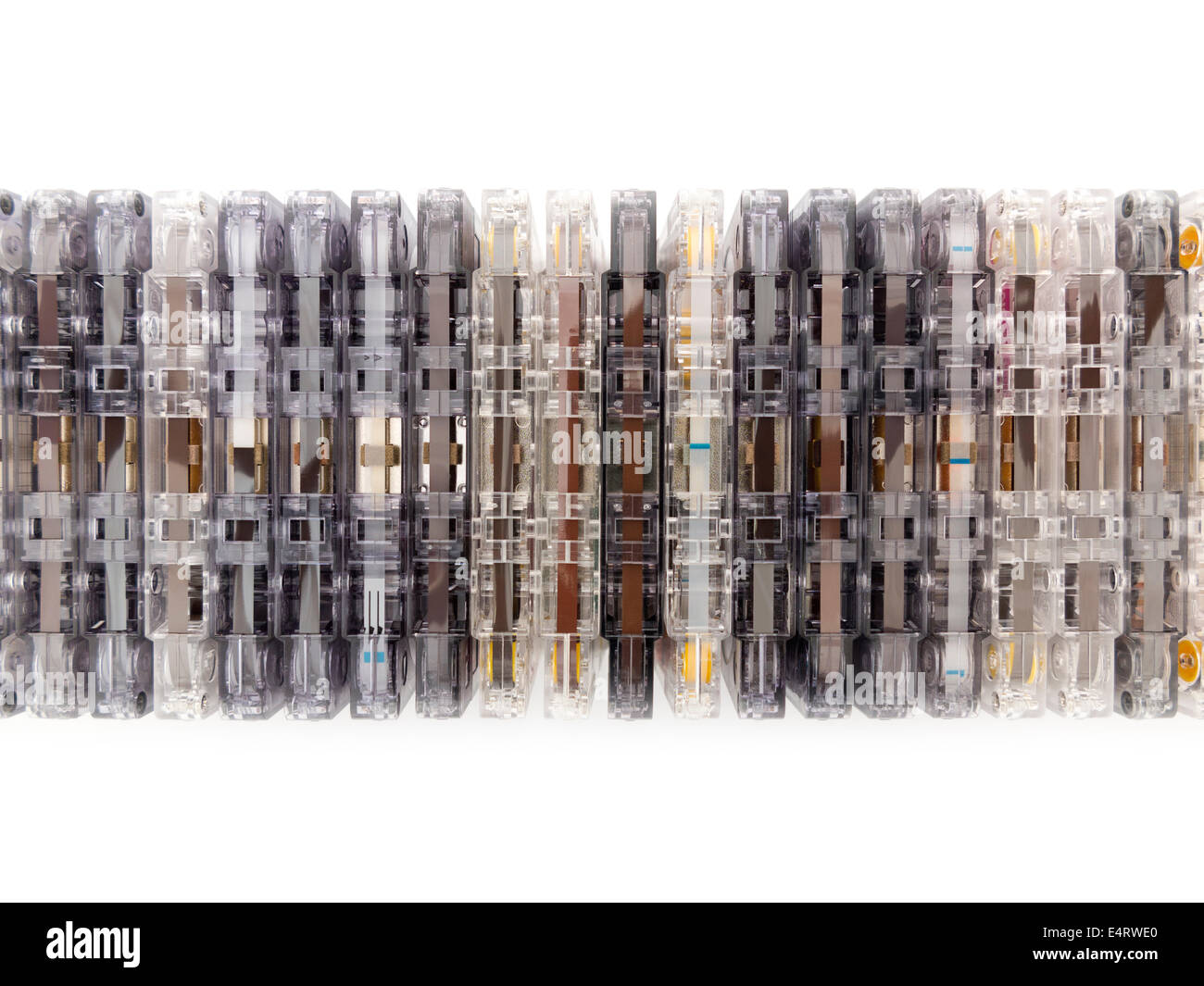 Una fila impilata di miste di compact cassette audio sul bordo, alcuni mostrano un nastro, altri leader di nastro, il tutto in una varietà di colori Foto Stock