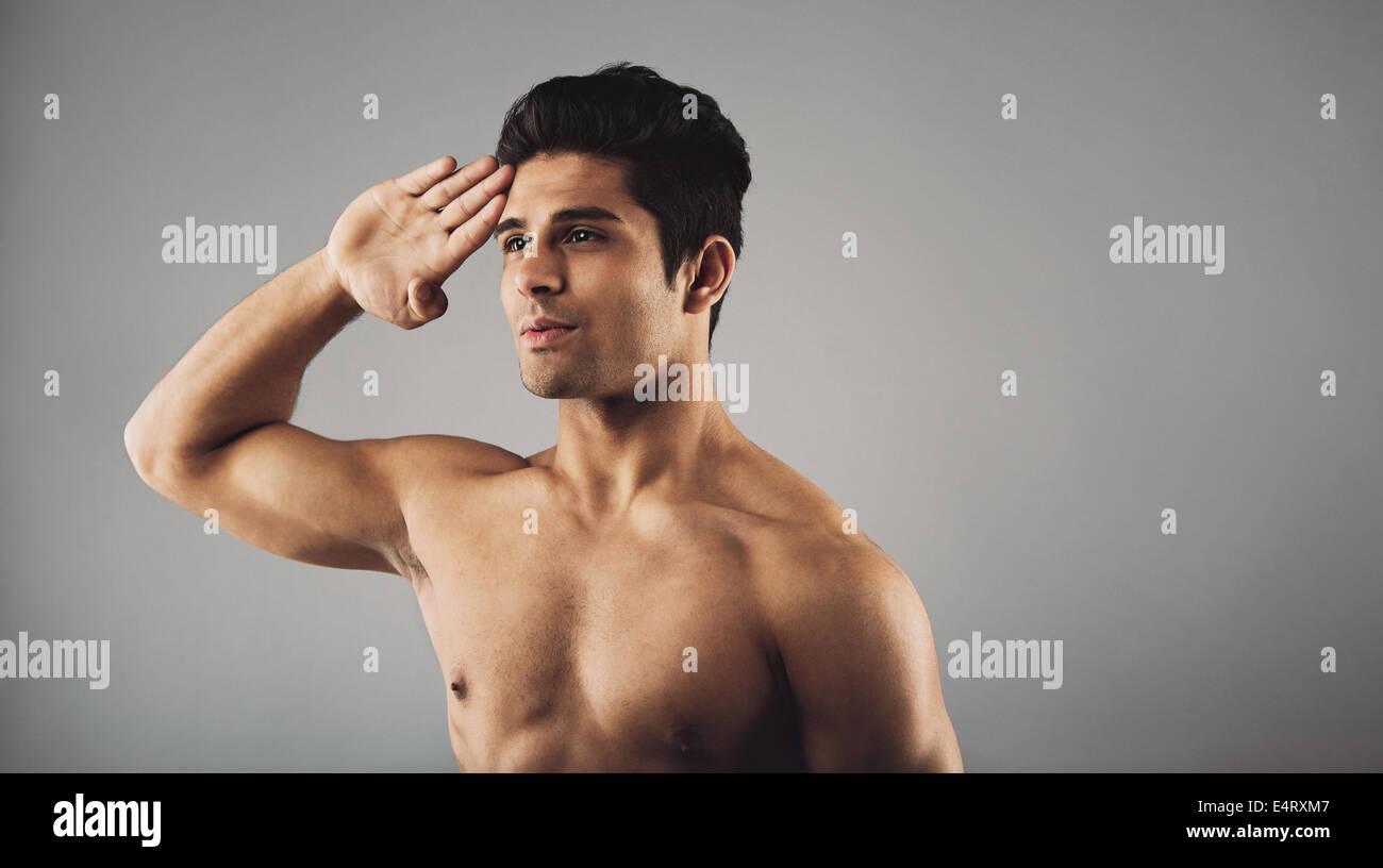 Ritratto di giovane uomo muscolare salutando. Il maschile giovane uomo facendo un saluto su sfondo grigio con copyspace. Foto Stock