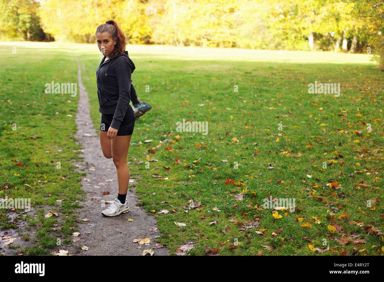 Bella giovane donna lo stiramento dei muscoli delle gambe durante gli allenamenti nel parco. Piuttosto giovane femmina caucasica runner il riscaldamento per un'esecuzione. Foto Stock
