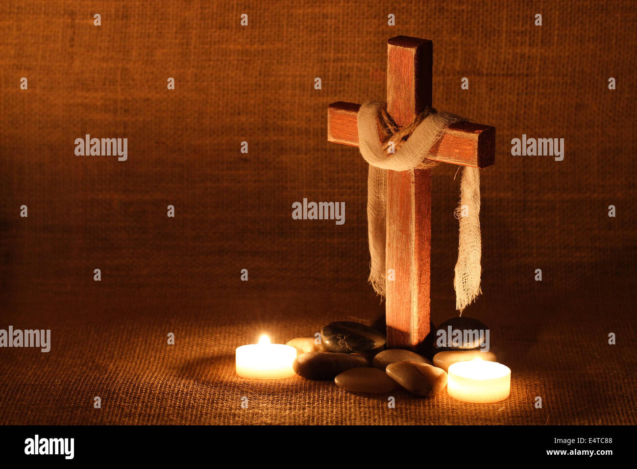 Croce di legno con panno drappeggiato a lume di candela e pietre con sfondo squallido Foto Stock