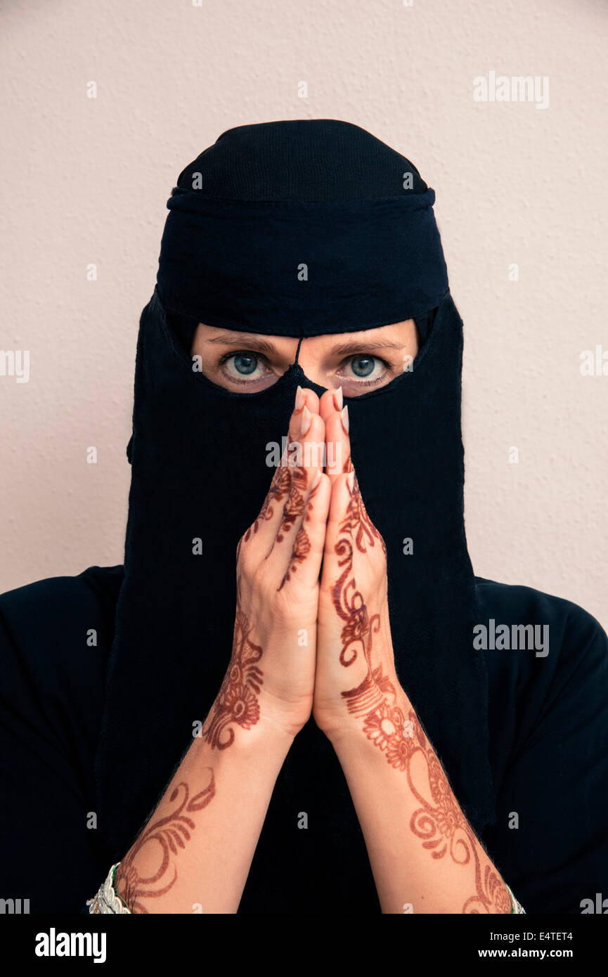 Ritratto di donna in nero musulmano hijab e abiti musulmani, mani pregando e verniciati con colore henné in stile arabo Foto Stock