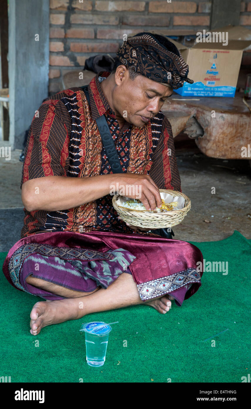 Bali, Indonesia. Balinese uomo indù e mangiare del riso. Indossa il udeng, il tradizionale Balinese panno di testa. Foto Stock