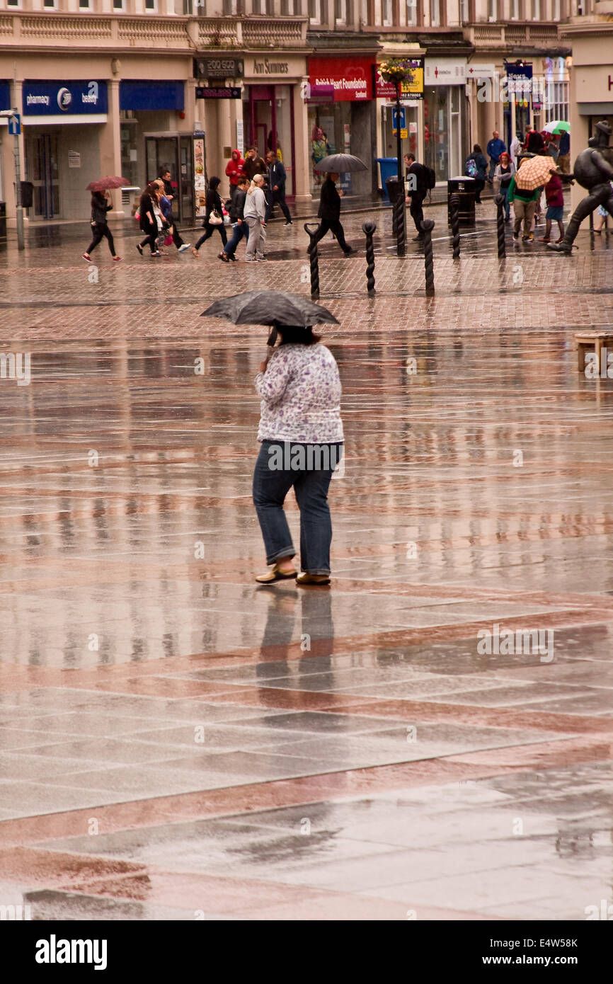 Le riflessioni di una donna il ricovero sotto un ombrello a piedi nel centro della città mentre la pioggia è il rizzaggio di Dundee, Regno Unito Foto Stock