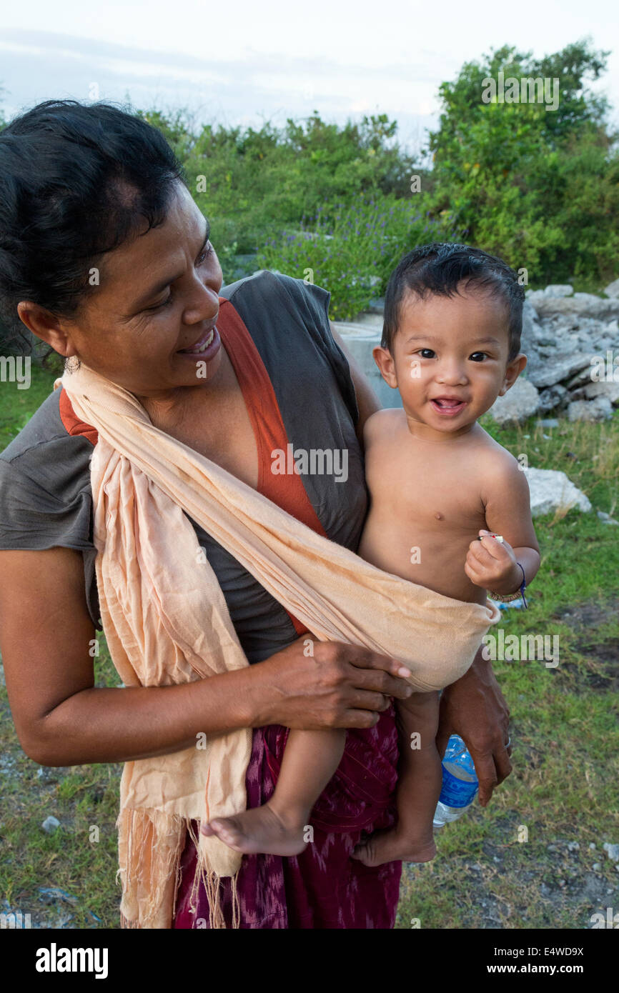 Bali, Indonesia. La madre che porta il figlio in una imbracatura spalla. Foto Stock