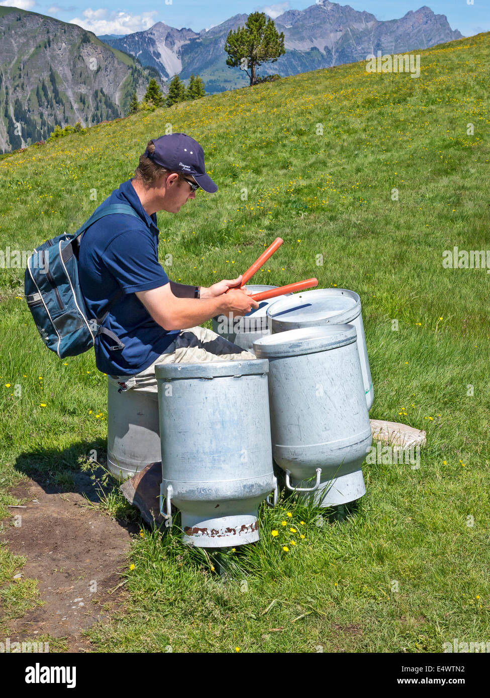 Un uomo giocando capovolta bidoni di latte come tamburi in una Svizzera prato alpino. Foto Stock