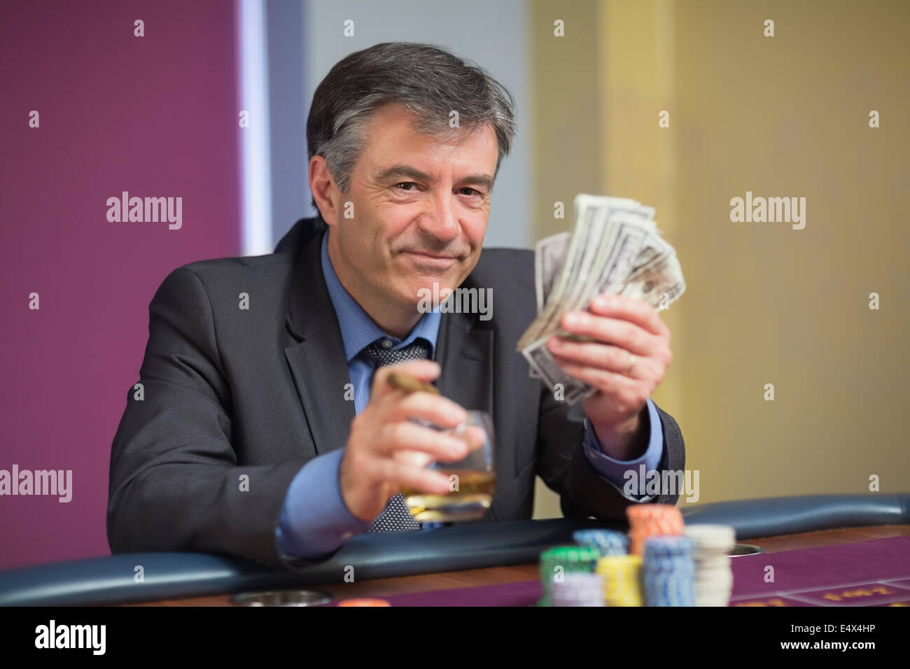 Uomo con denaro sorridente al tavolo della roulette Foto Stock