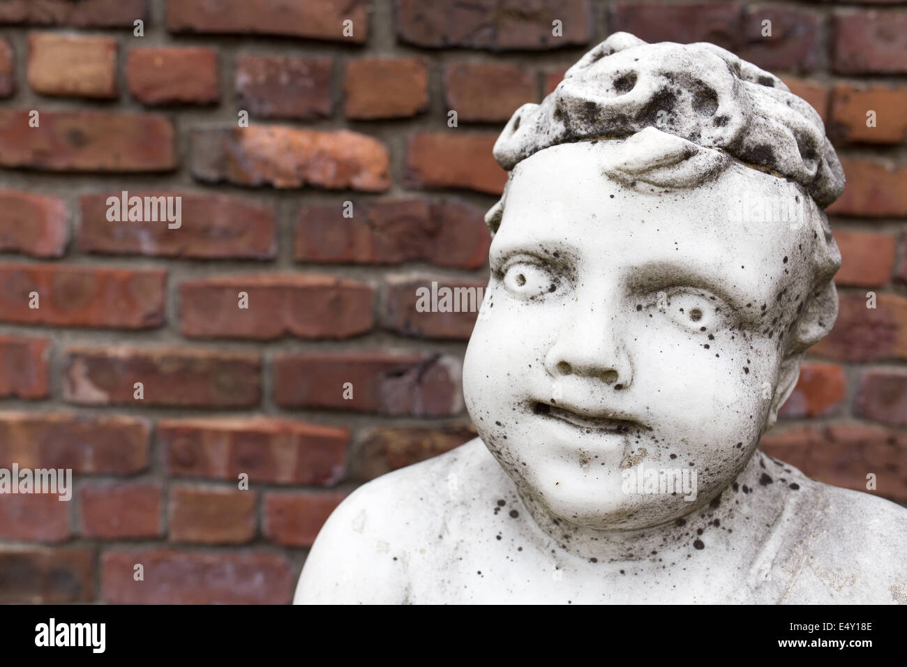 Una vecchia statua in marmo bianco di un cherubino ragazzo contro un muro del giardino con spazio di copia. Foto Stock