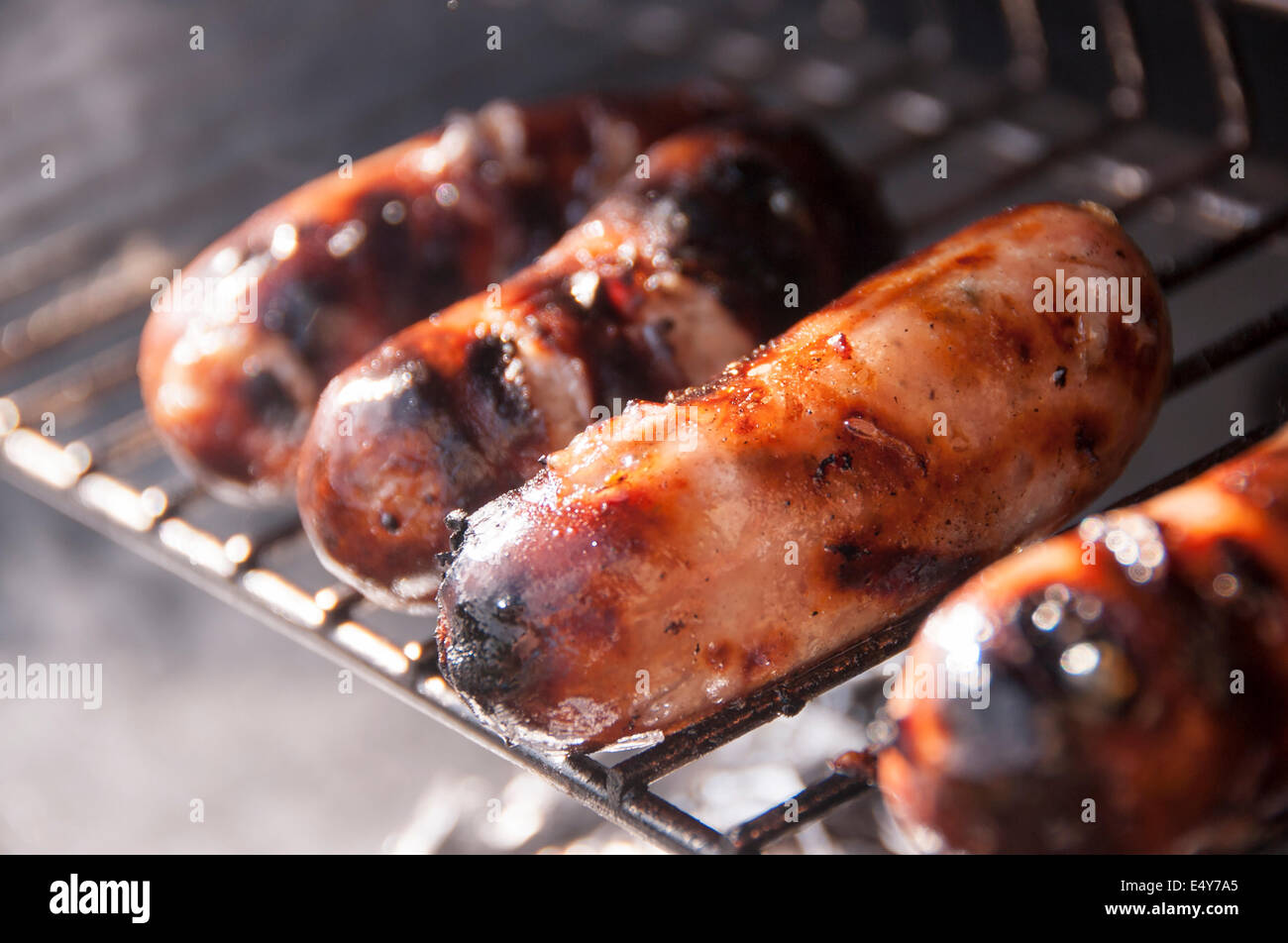 Salsicce cottura su una griglia per il barbecue, sfrigolante e fumare fuori nel sole Foto Stock