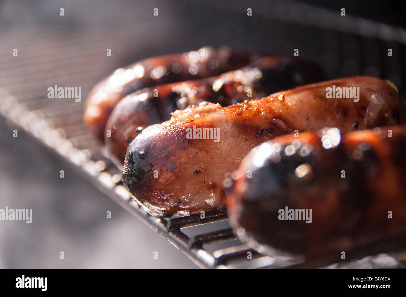 Salsicce cottura su una griglia per il barbecue, sfrigolante e fumare fuori nel sole Foto Stock
