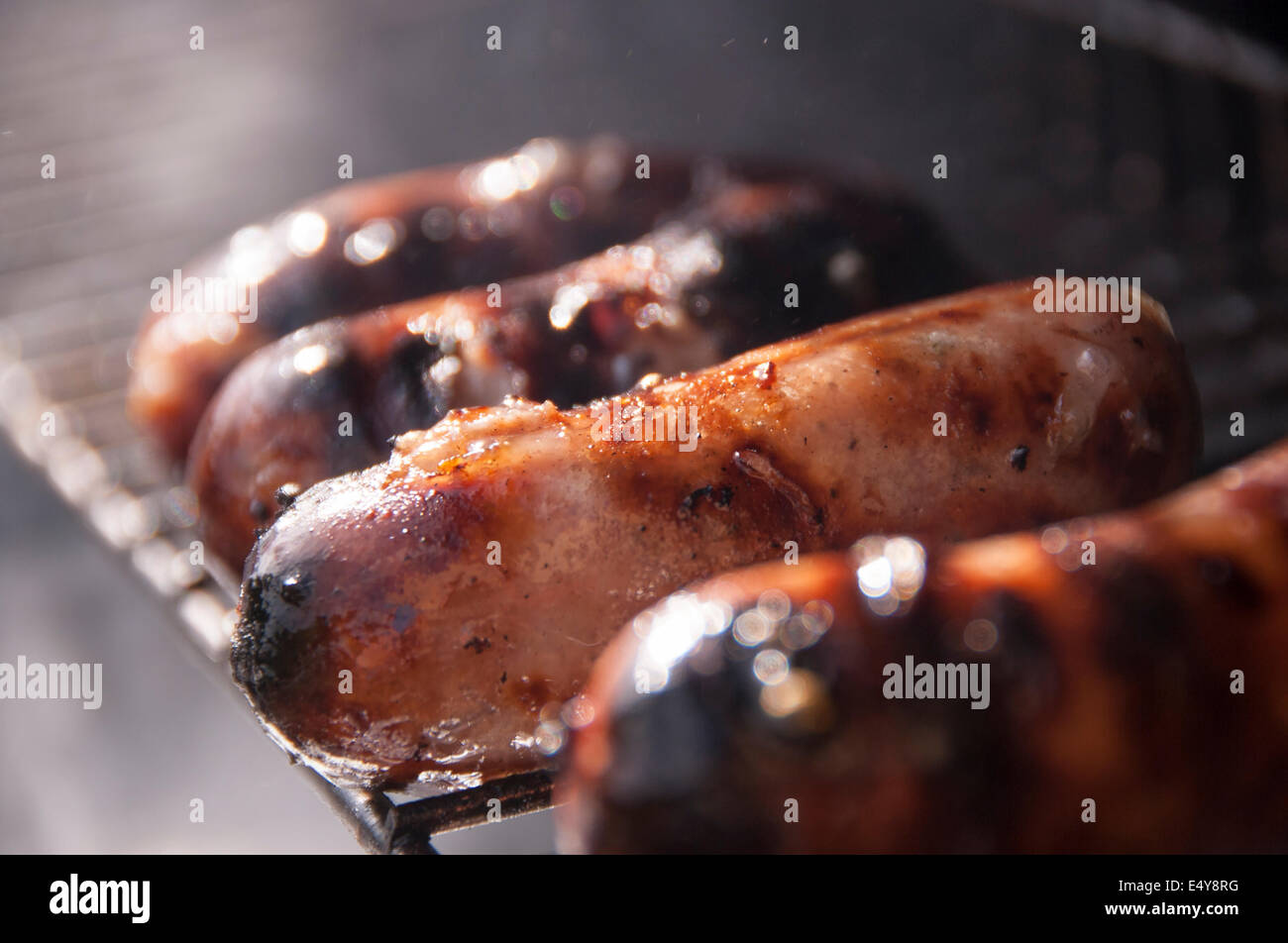 Salsicce cottura su una griglia per il barbecue, sfrigolante e fumare fuori nel sole Foto Stock