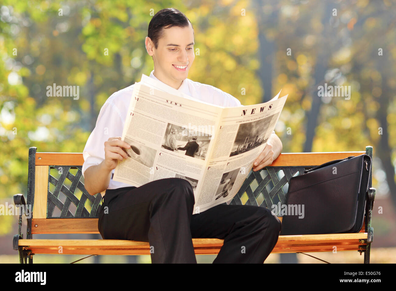 Imprenditore seduto su una panchina leggendo un giornale in un parco Foto Stock