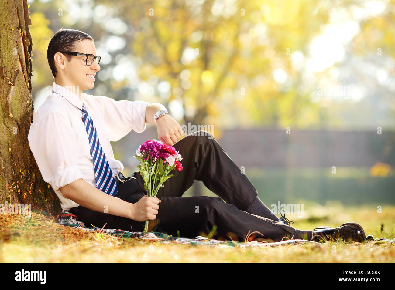 Giovane uomo con il mazzo di fiori in seduta su una erba e controllando il tempo in un parco Foto Stock