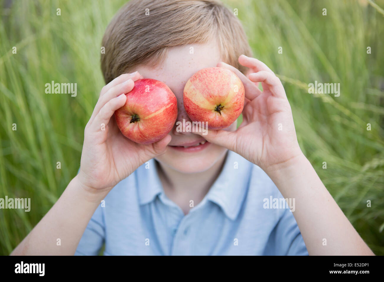 Un ragazzo tenendo due red scuoiati mele oltre i suoi occhi. Foto Stock