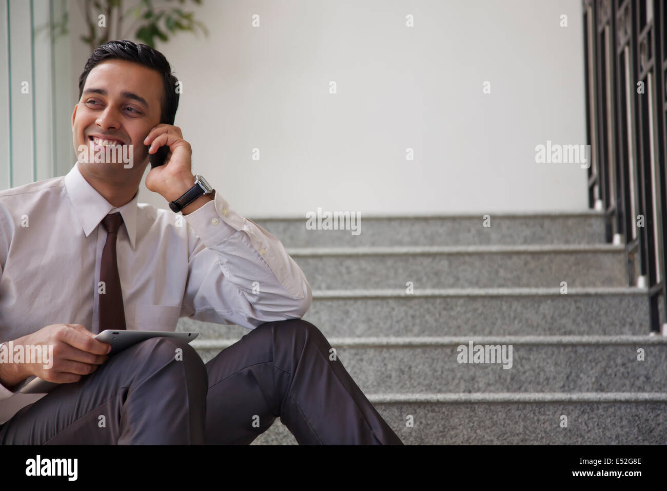 Executive maschio con la compressa a parlare su un telefono mobile Foto Stock