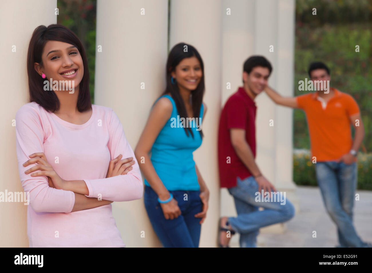 Ritratto di donna sorridente e amici che poggiano su colonne all'aperto Foto Stock