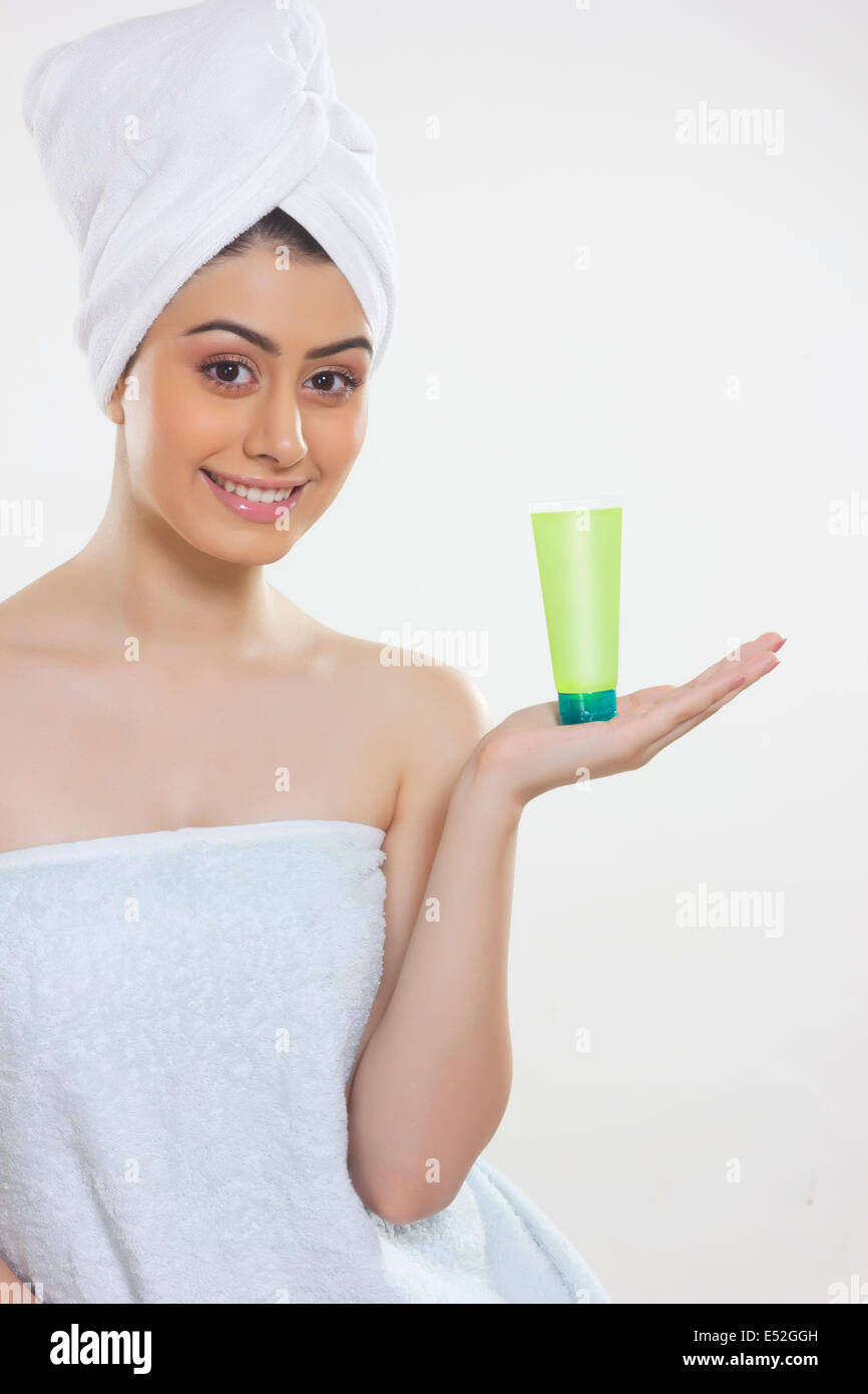 Ritratto di donna bella avvolto in asciugamano che mostra prodotto di bellezza contro uno sfondo bianco Foto Stock