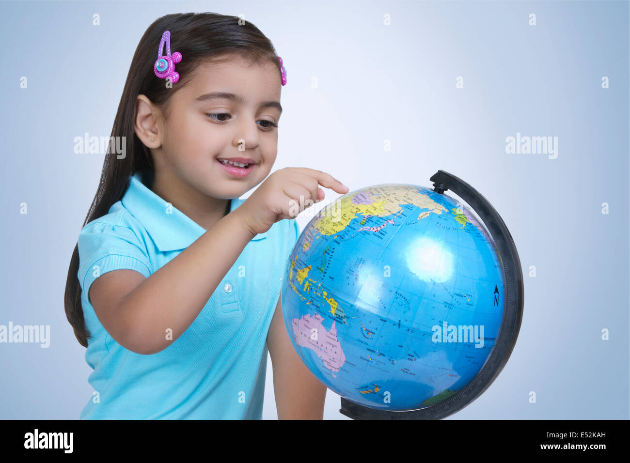 Ragazza sorridente esplorare globe contro sfondo blu Foto Stock