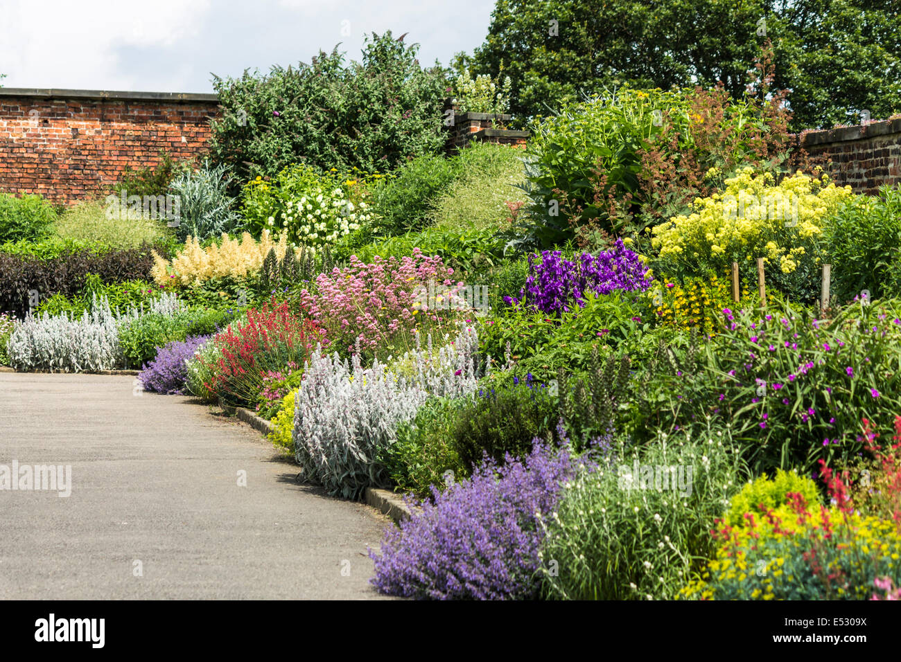 Bellissimo giardino fiorito con un muro di mattoni in una giornata di sole Foto Stock