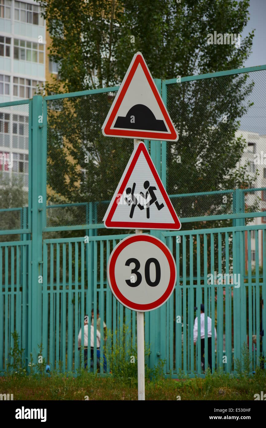Tre indicazioni stradali su un polo: ostacolo artificiale, attentamente i bambini, limite di velocità 30 - con una scuola e parco giochi bambini Foto Stock
