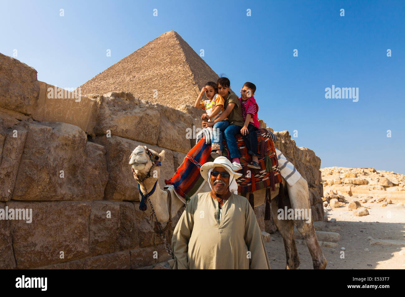 Driver di cammello con bambini mediante la Grande Piramide. Il Cairo, Egitto Foto Stock