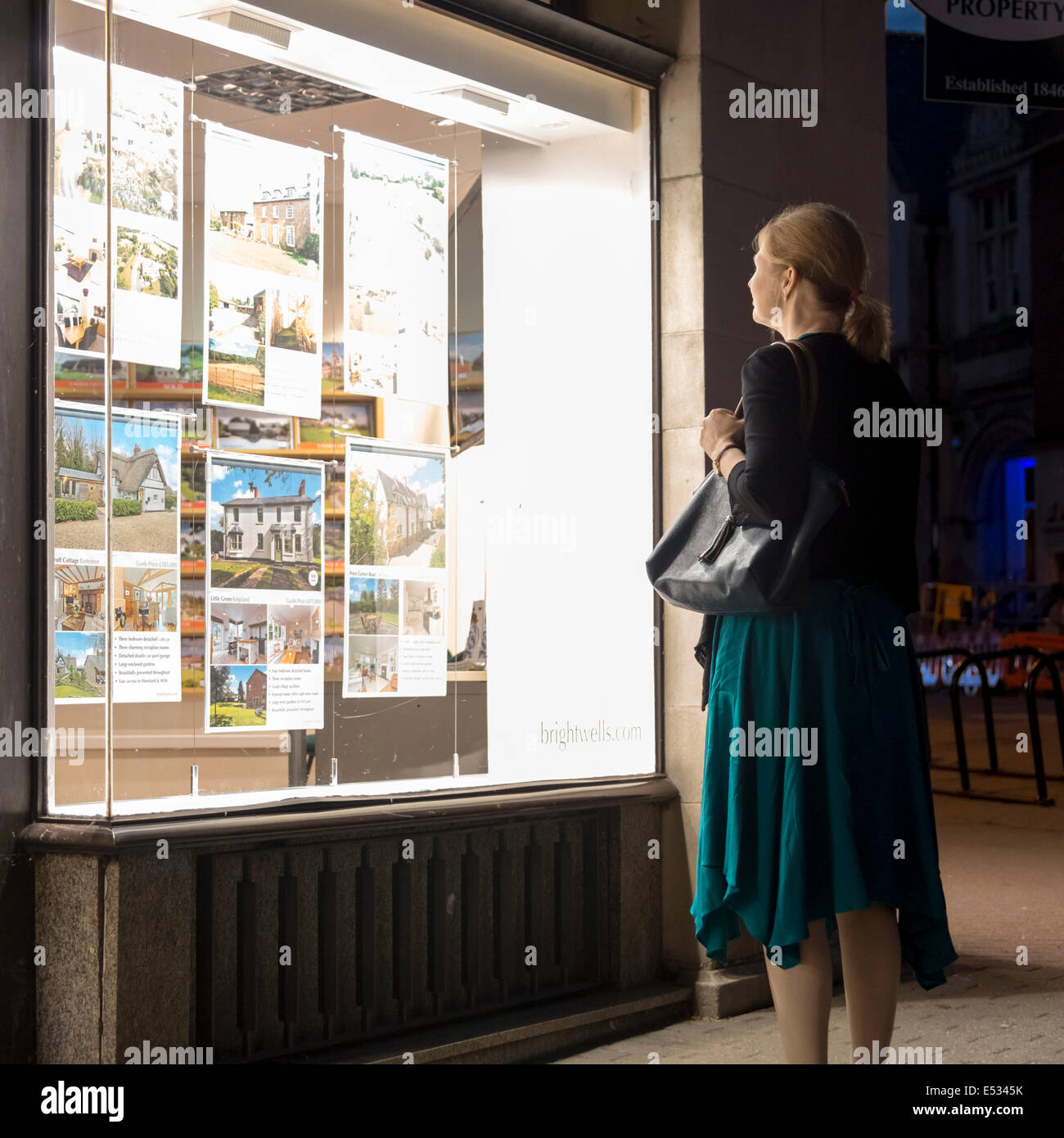 Donna che guarda in un agenti immobiliari finestra la notte, UK. Foto Stock