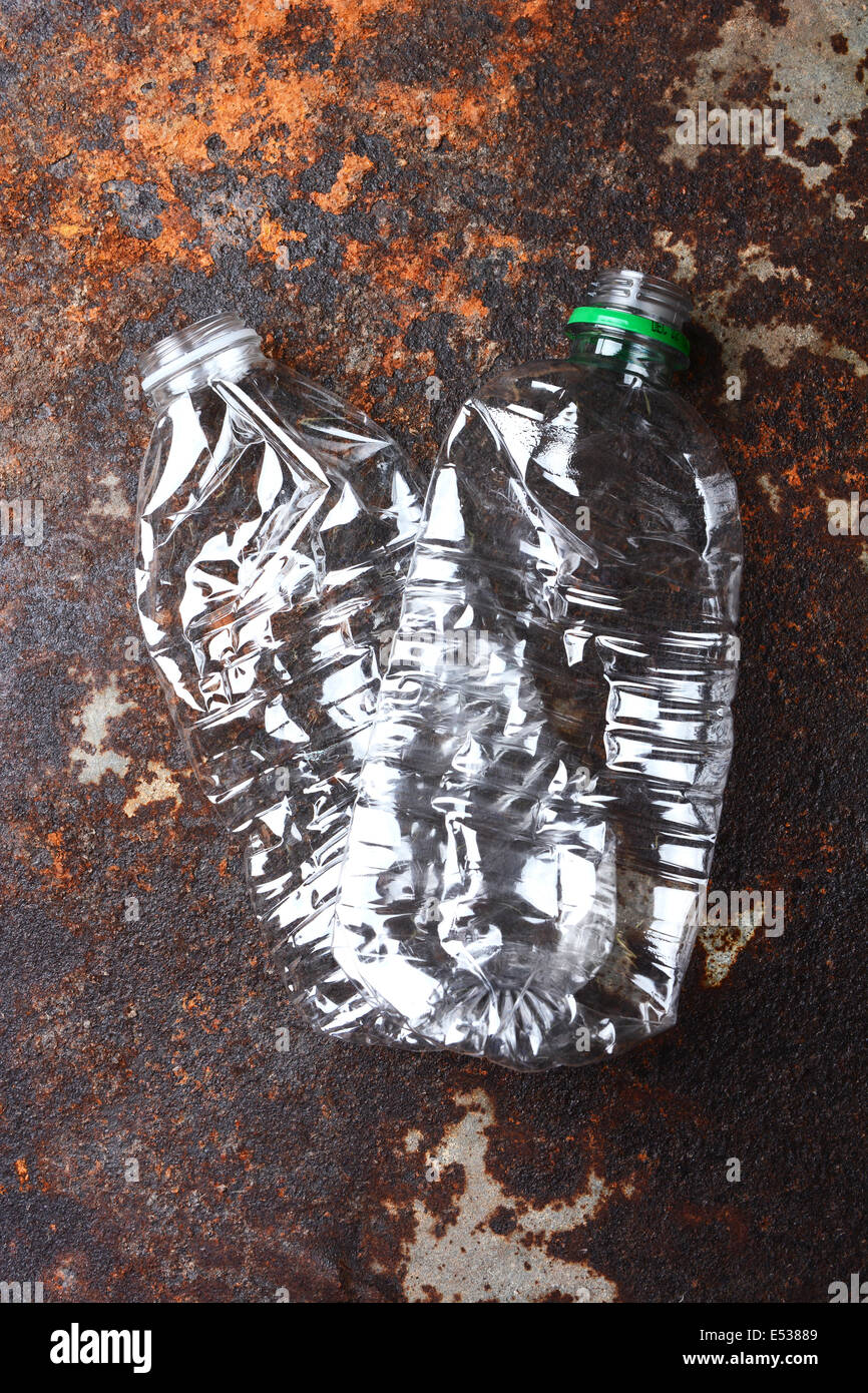 Primo piano di due schiacciate e scartato in plastica bottiglie di acqua su un metallo arrugginito superficie. Elevato angolo girato con una forte luce laterale. Foto Stock