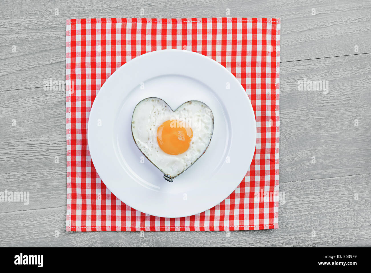 Uovo fritto a forma di cuore sulla tavola vintage. La prima colazione per una persona amata Foto Stock