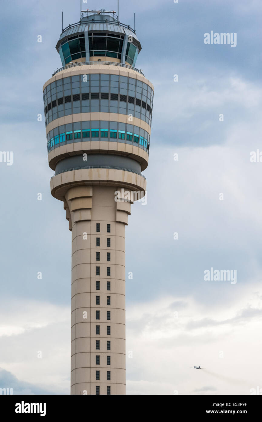 Il sistema di controllo del traffico aereo torre sorge sentinella sul Atlanta International Airport come un jet del passeggero si arrampica in un cielo nuvoloso. Foto Stock
