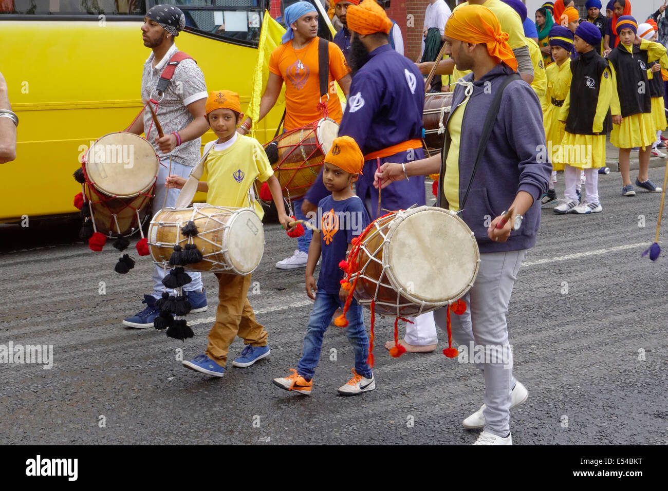 Middlesbrough, Regno Unito. Il 20 luglio, 2014. L annuale Nagar Kirtan Parade celebra la cultura Sikh nel nord-est dell' Inghilterra ha avuto luogo in Middlesbrough Cleveland UK oggi è domenica 20 luglio. Il corteo è guidato da cinque zafferano derubato gli uomini che portano un galleggiante che porta il Guru Granth Sahib i sikh la Sacra Scrittura. Membri della processione è a piedi nudi in ossequio alla scrittura così visualizzato. Essi sono preceduti da spazzatrici pulizia della strada. Questa immagine mostra la religione Sikh ragazzi marciando e suonando la batteria in parata Credito: Pietro Giordano NE/Alamy Live News Foto Stock