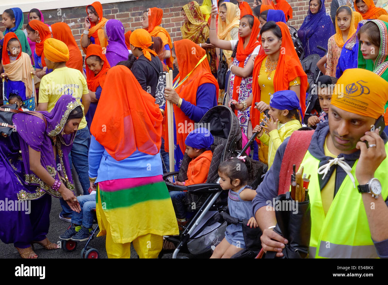 Middlesbrough, Regno Unito. Il 20 luglio, 2014. L annuale Nagar Kirtan Parade celebra la cultura Sikh nel nord-est dell' Inghilterra ha avuto luogo in Middlesbrough Cleveland UK oggi è domenica 20 luglio. Il corteo è guidato da cinque zafferano derubato gli uomini che portano un galleggiante che porta il Guru Granth Sahib i sikh la Sacra Scrittura. Membri della processione è a piedi nudi in ossequio alla scrittura così visualizzato. Essi sono preceduti da spazzatrici pulizia della strada. Questa immagine mostra i sikh famiglie pronte a seguire il galleggiante sul retro della sfilata Credito: Pietro Giordano NE/Alamy Live News Foto Stock