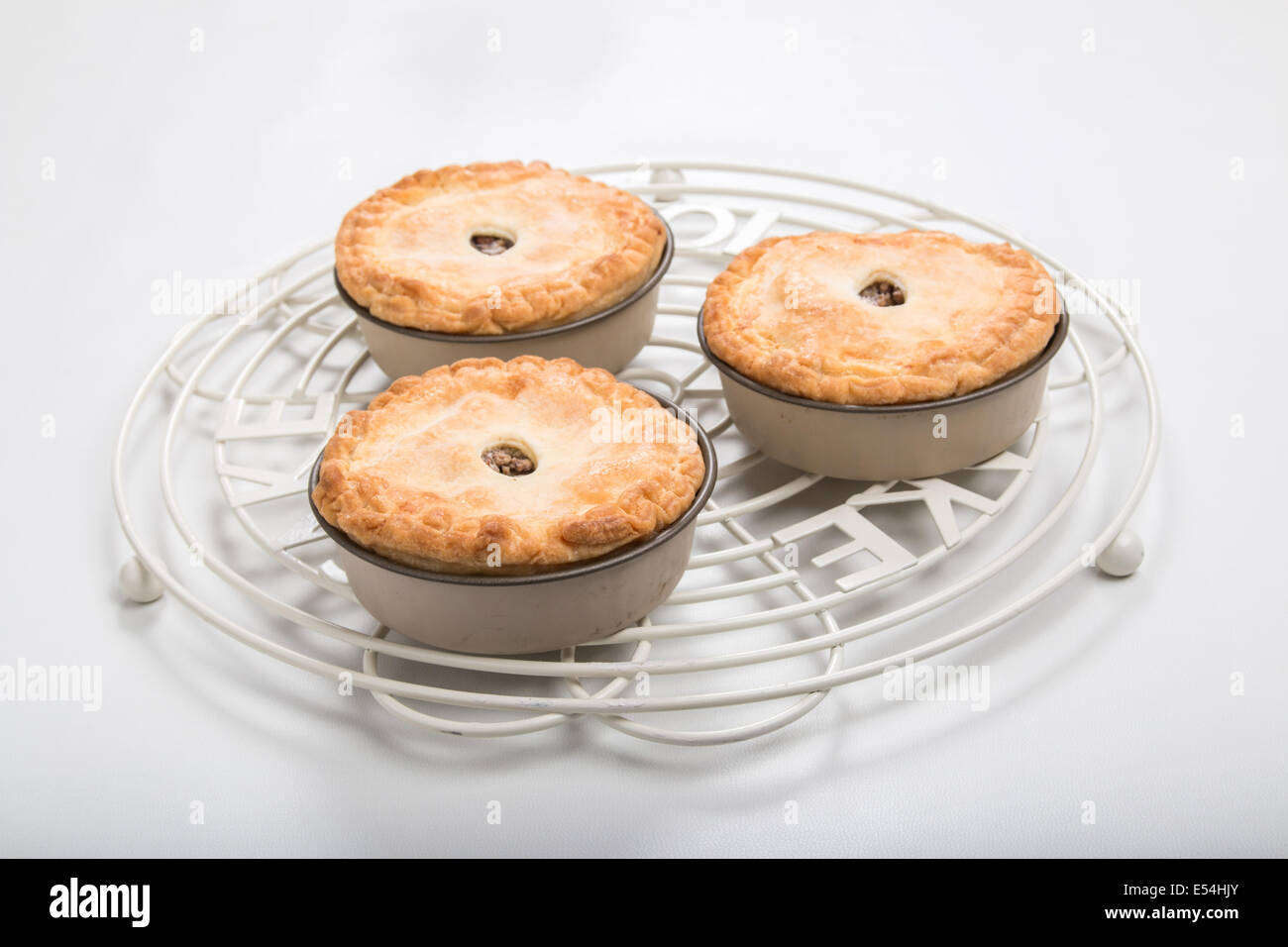 3 piccoli pasticci di carne in teglie su un giro di raffreddamento per rack su uno sfondo chiaro singoli torte adatto per un picnic (12 di 20 ) Foto Stock