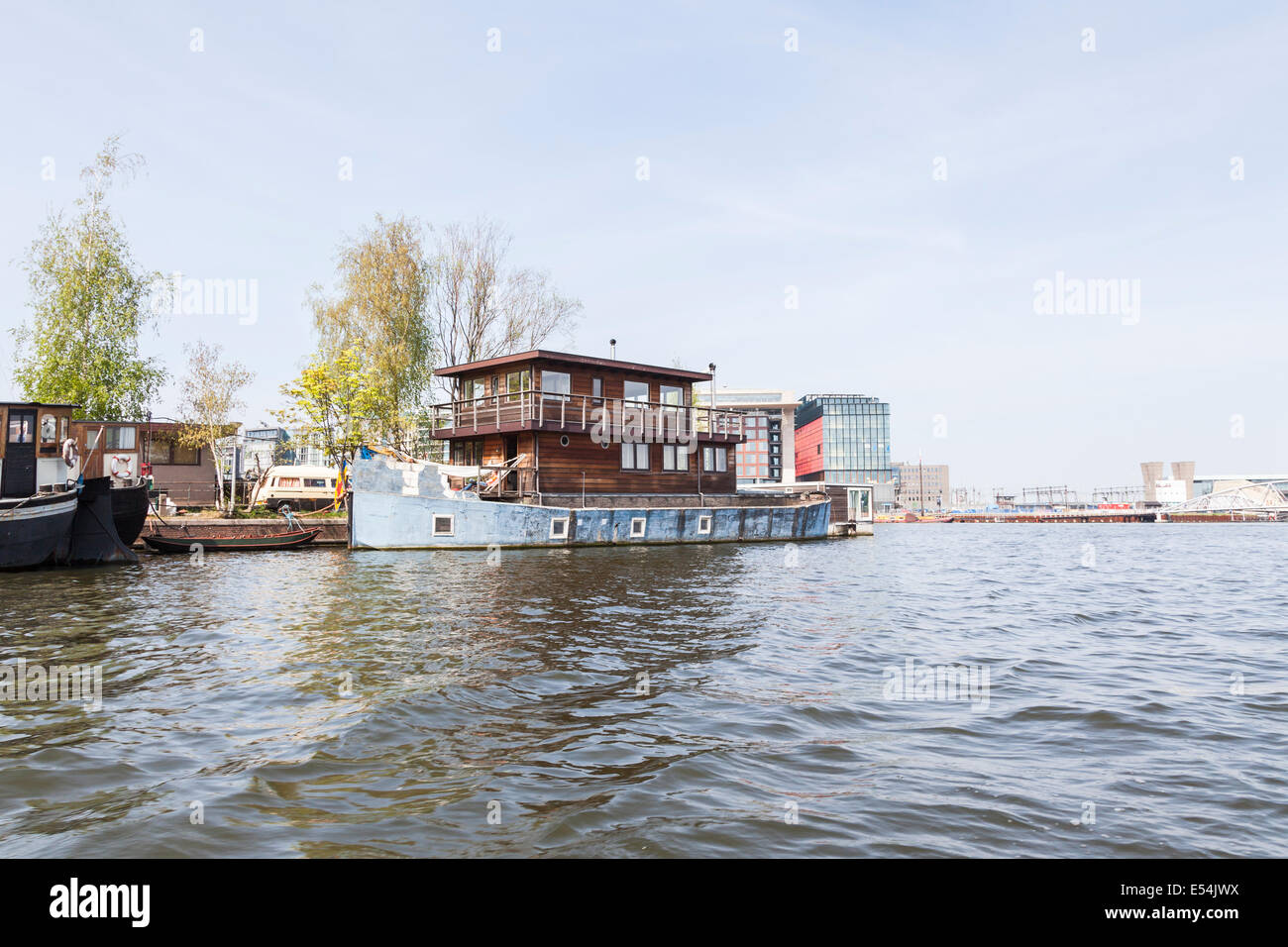 Casa insolita ormeggiata sulla riva di un canale di Amsterdam: casa in legno con una base in muratura, all'interno dello scafo di una barca blu Foto Stock