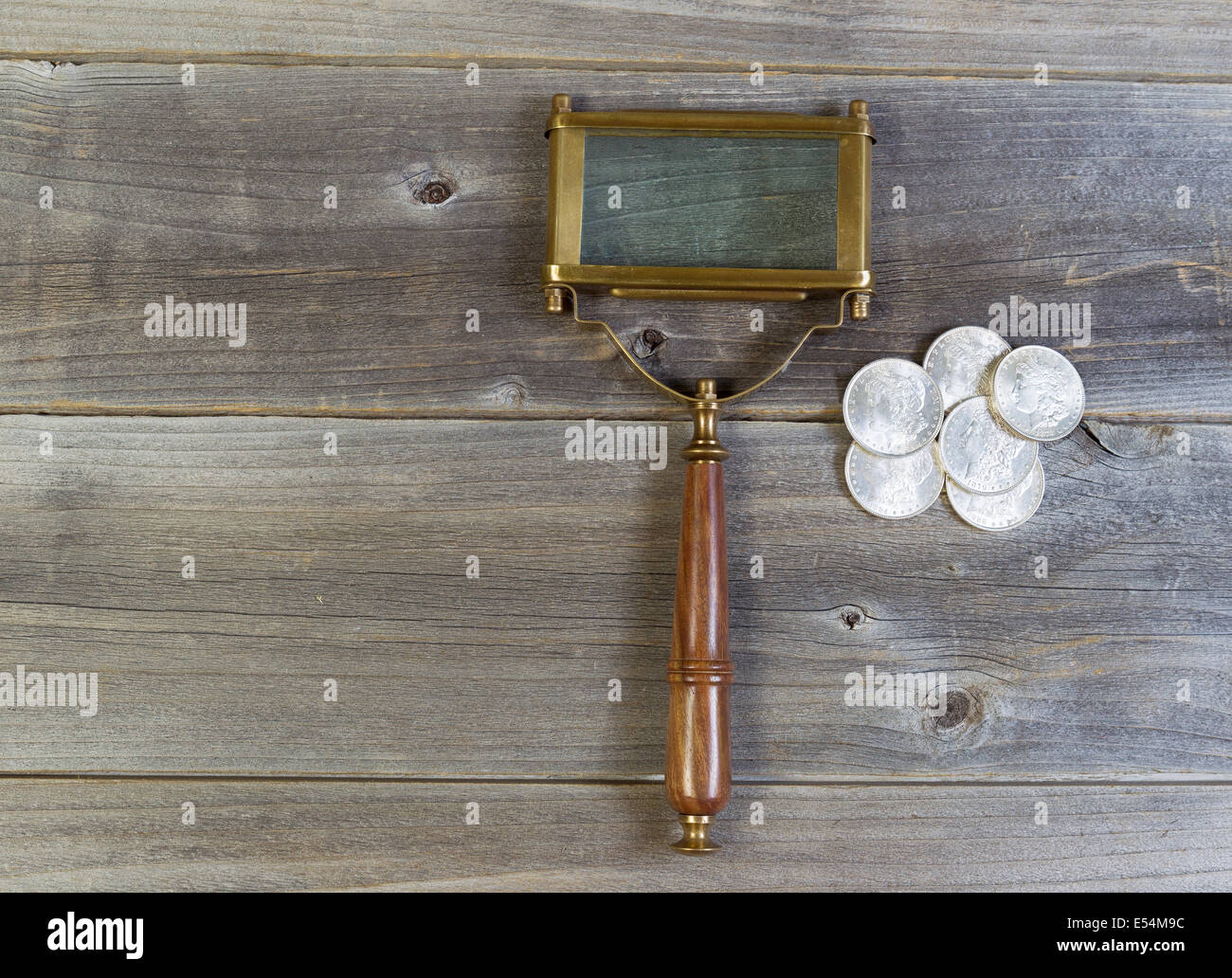 Vista orizzontale di un vecchio di forma rettangolare a forma di lente di ingrandimento e di una pila di vecchi silver dollar monete sul legno rustico Foto Stock