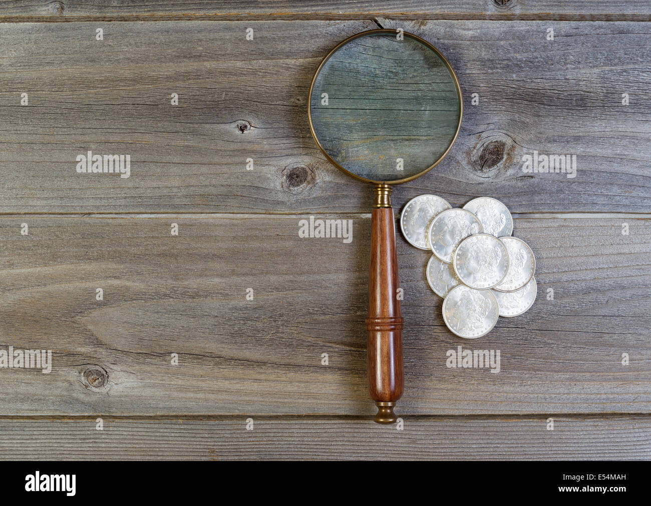 Vista orizzontale di un antico round a forma di lente di ingrandimento e di una pila di vecchi silver dollar monete sul legno rustico Foto Stock