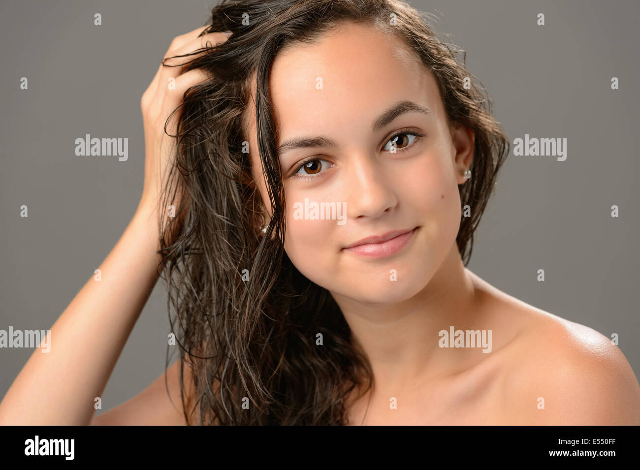 Ragazza adolescente toccare i capelli bagnati Cosmetici cura su sfondo grigio Foto Stock