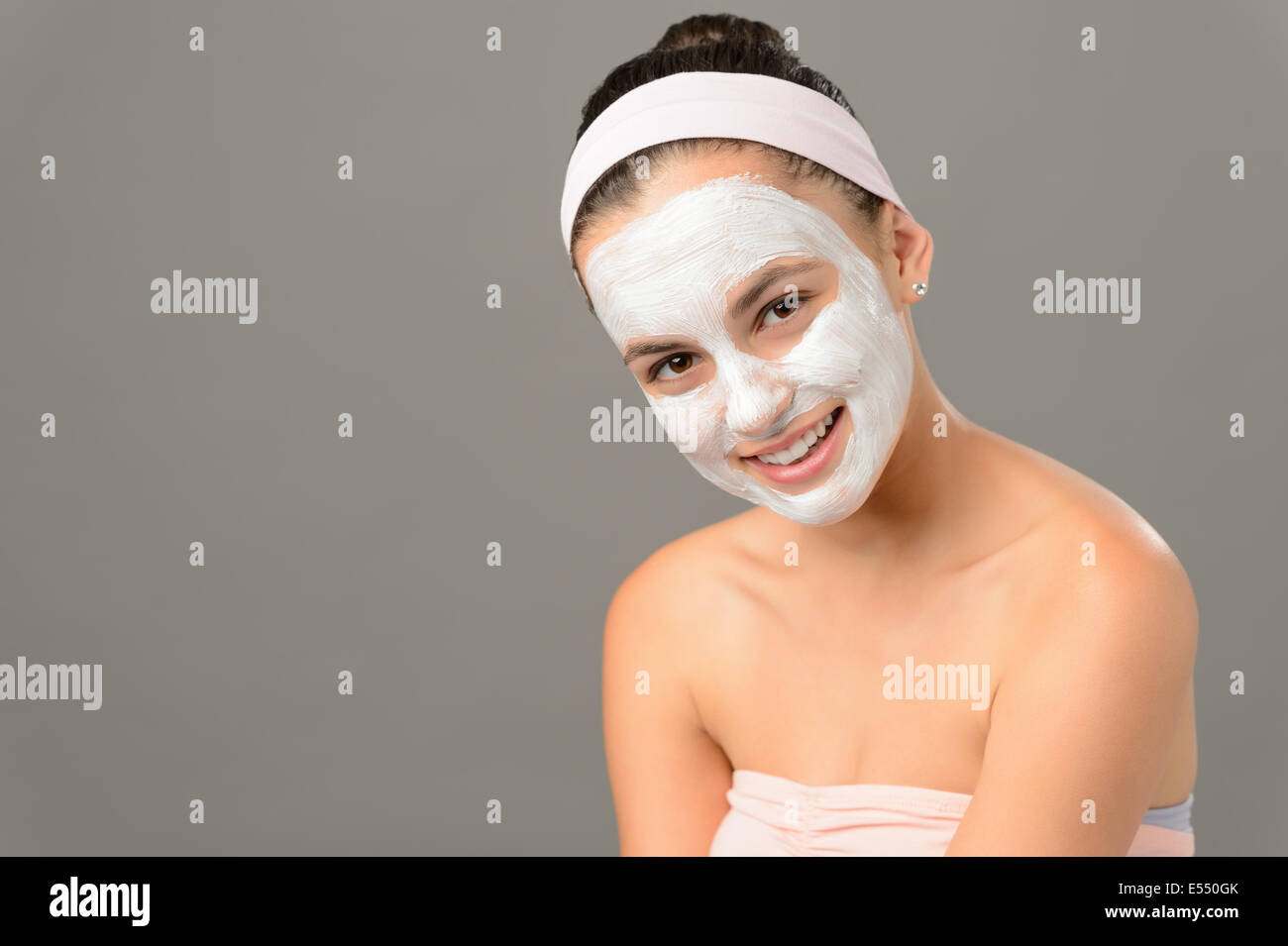 Sorridente ragazza adolescente maschera cosmetici bellezza della pelle su sfondo grigio Foto Stock