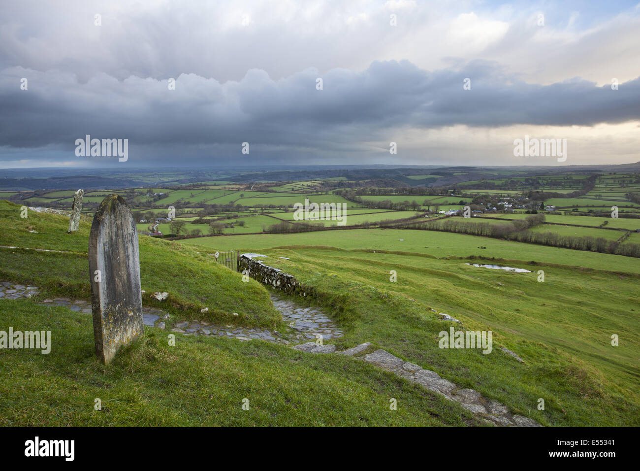 Vista del cimitero e il percorso che conduce dal XIII secolo la chiesa sulla brughiera di sunrise, con rainclouds sulle lontane campagna, Chiesa di San Michele, Brent Tor, Dartmoor N.P., Devon, Inghilterra, Dicembre Foto Stock