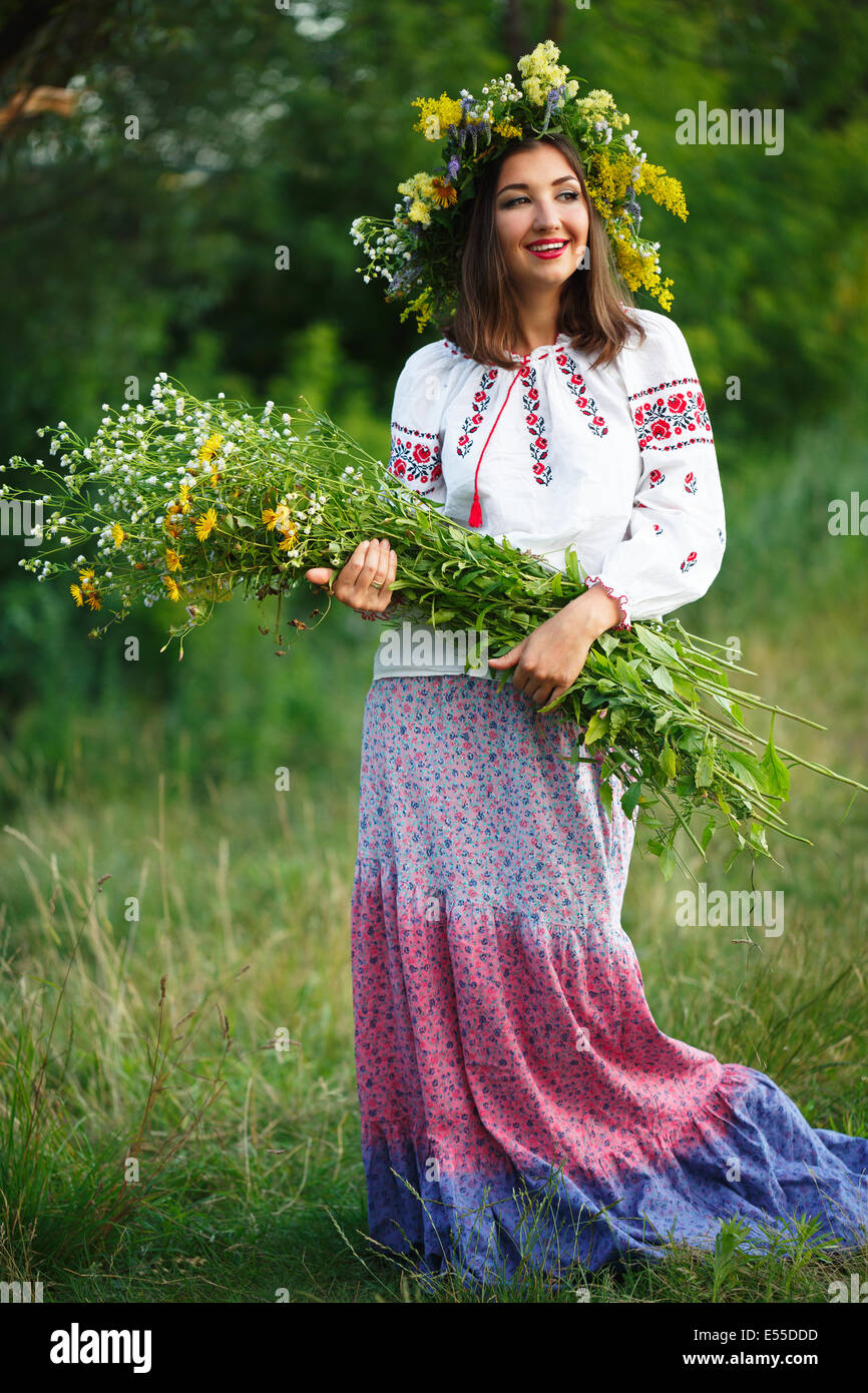 Giovane bella ragazza sorridente in ucraino costume con una corona di fiori alla sua testa in un prato Foto Stock